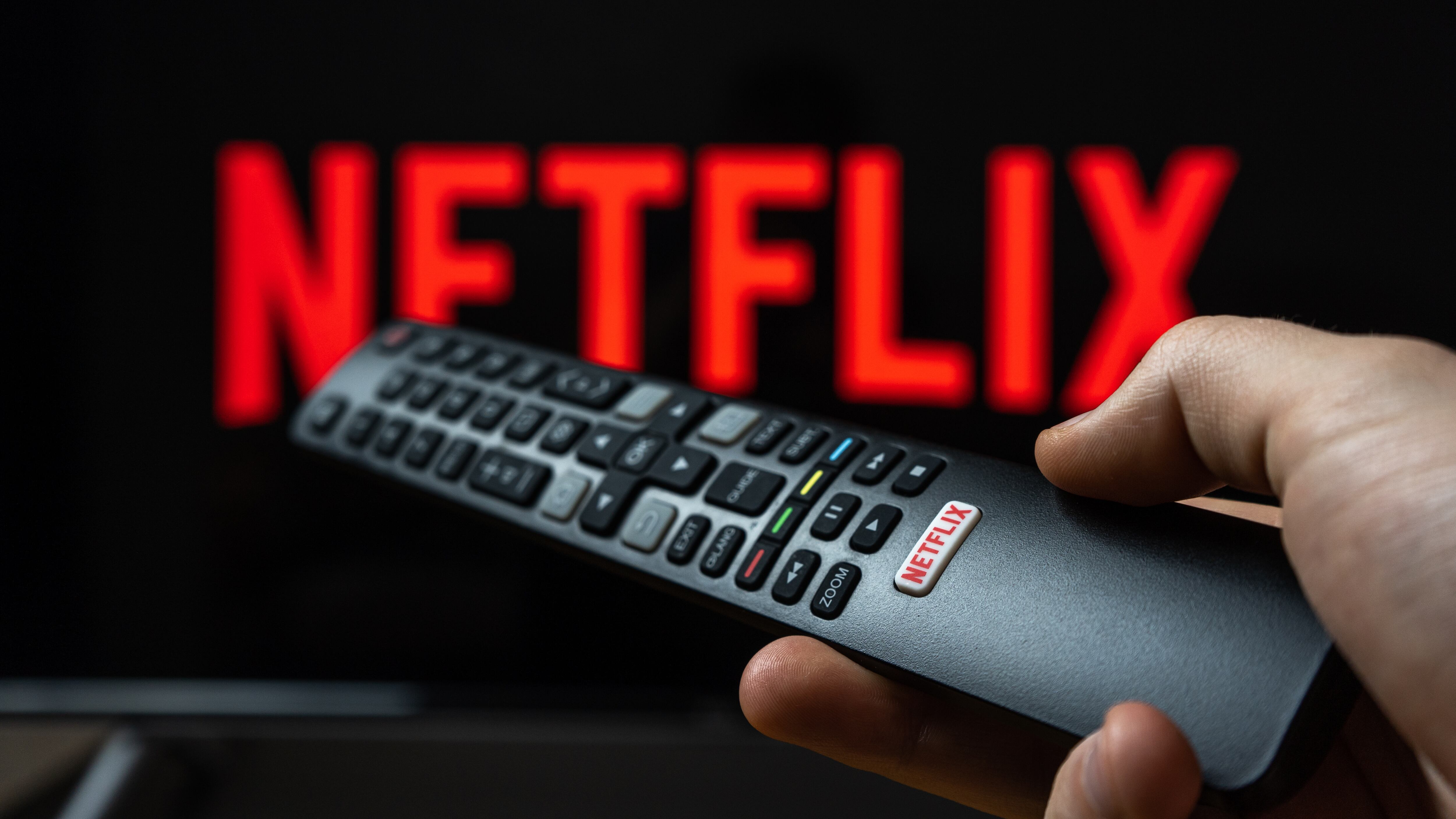 Holding TV remote controller with Netflix logo. Turning on Netflix platform on TV